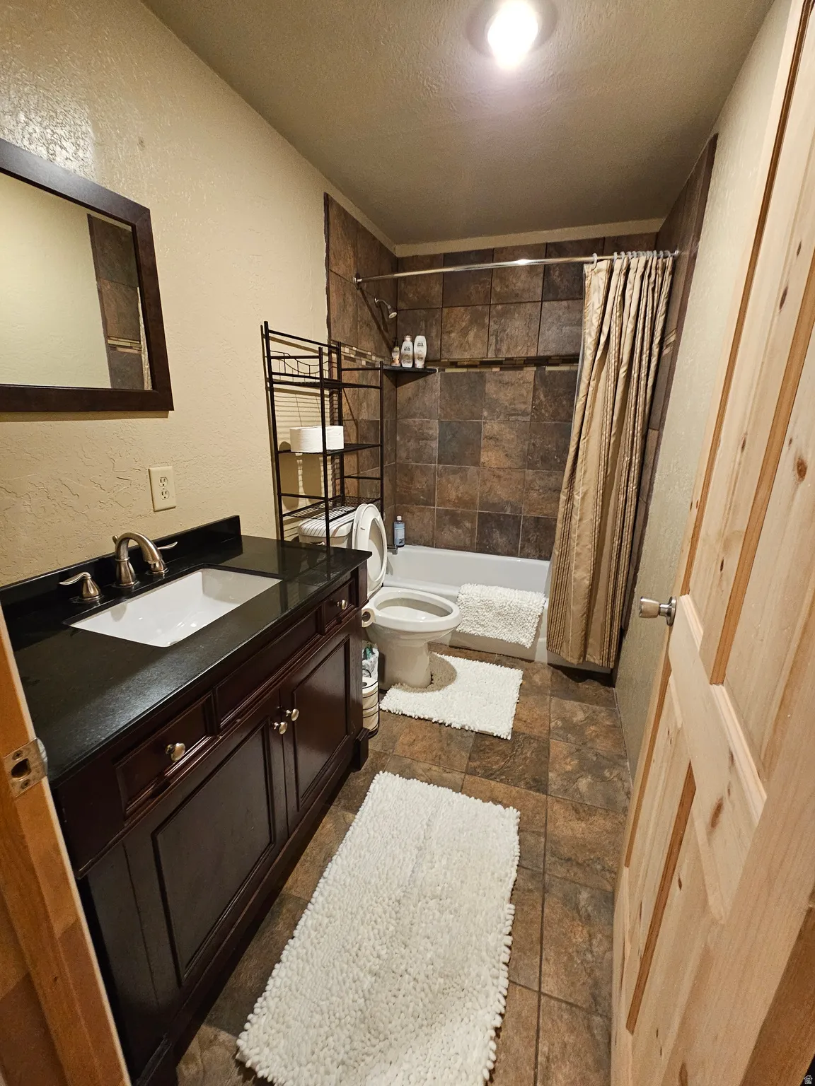 Bathroom with a textured wall, a textured ceiling, vanity, dark stone finish floors, and shower / bath combo