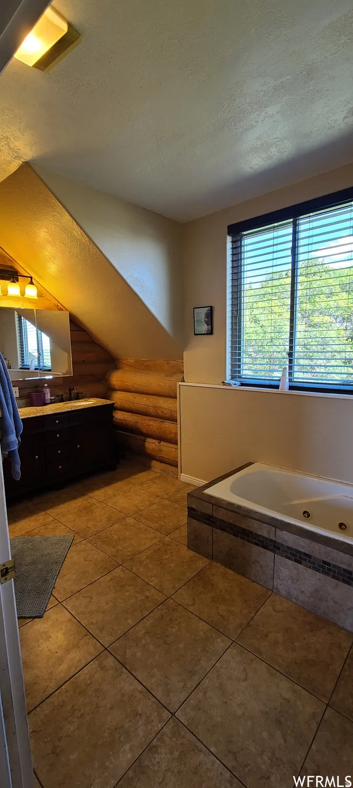 Bathroom with vanity, a jetted tub, dark tile patterned floors, and rustic walls
