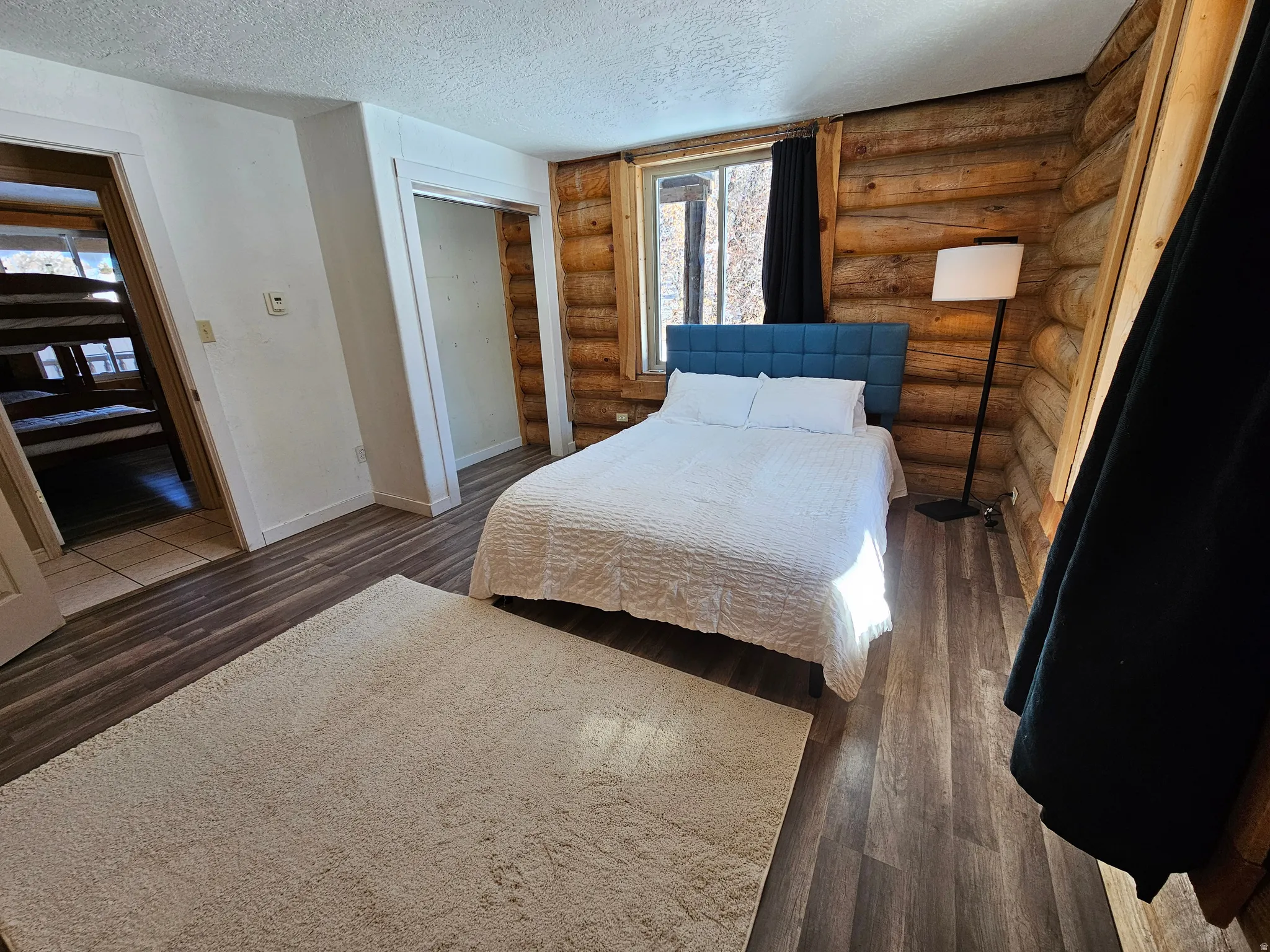 Bedroom with a textured ceiling, log walls, and dark wood finished floors