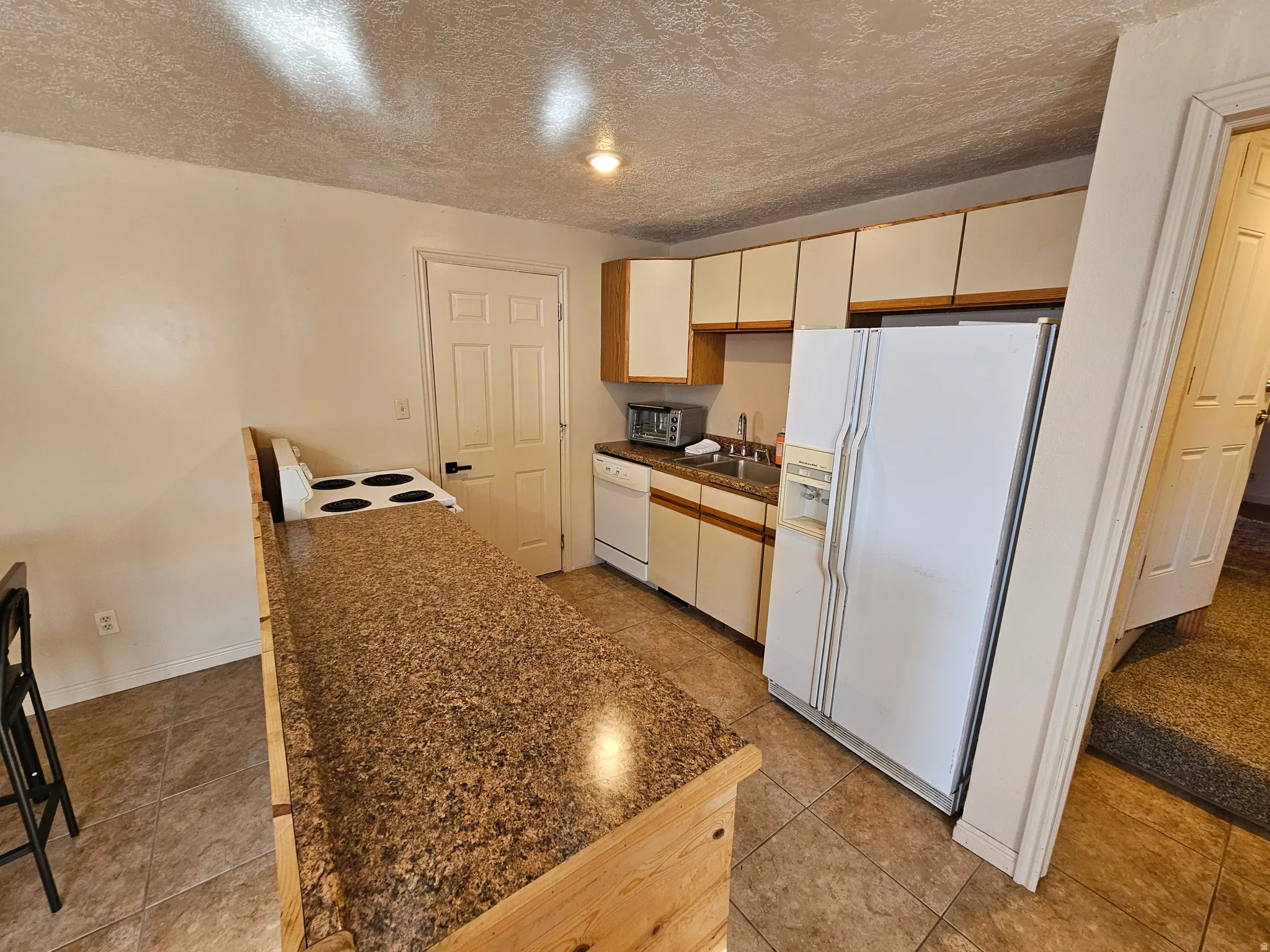 Kitchen with dark countertops, white appliances, a textured ceiling, and light tile patterned flooring