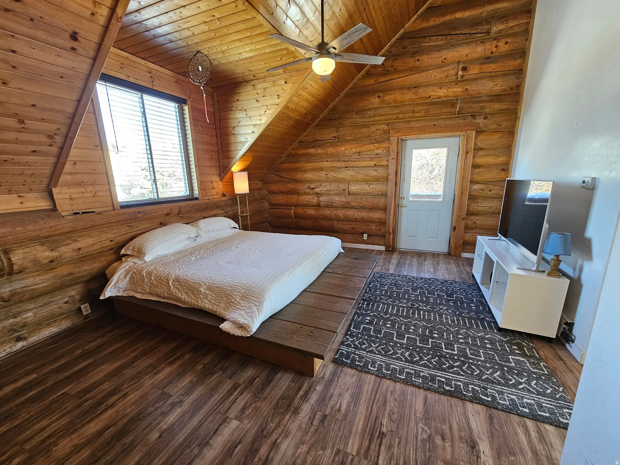 Bedroom with rustic walls, a vaulted wood ceiling, hardwood / wood-style floors, and a ceiling fan