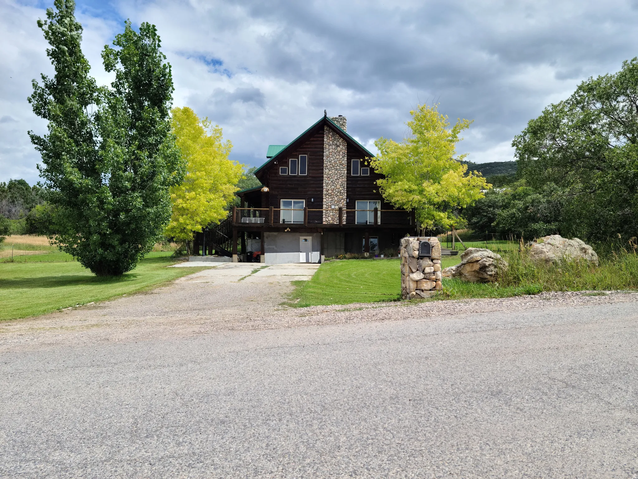Chalet / cabin with a wooden deck, an attached garage, driveway, a front lawn, and a chimney