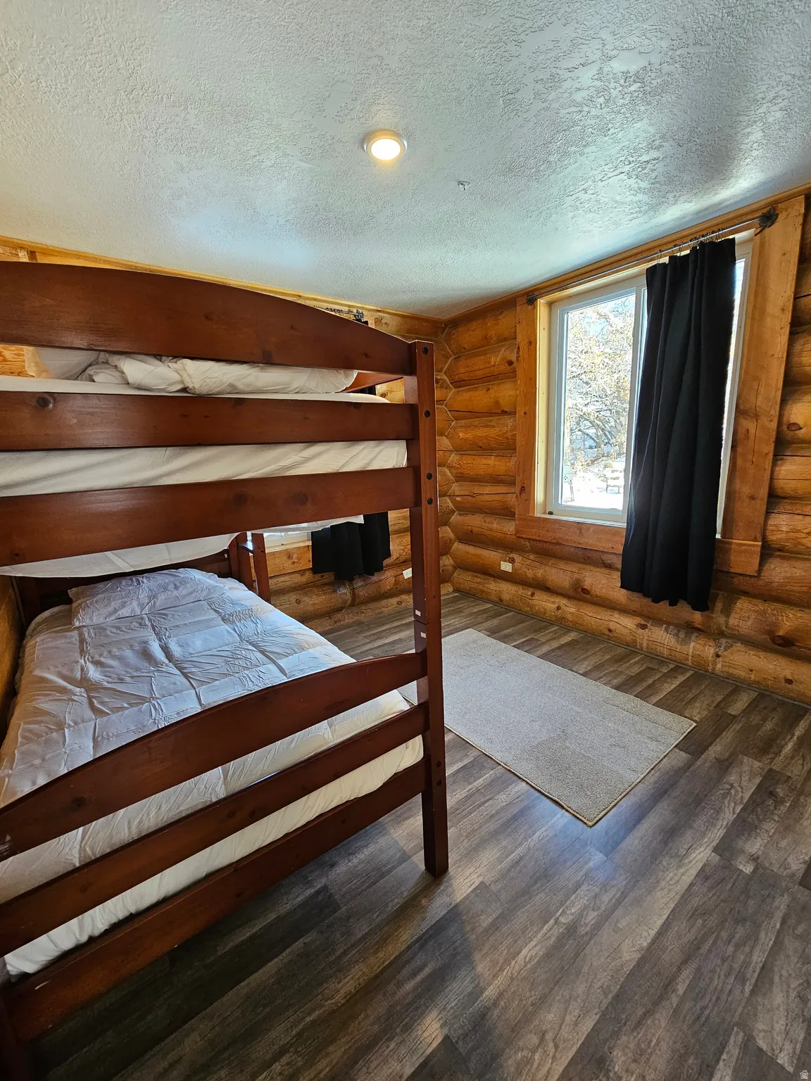 Bedroom with a textured ceiling, rustic walls, and dark wood-type flooring