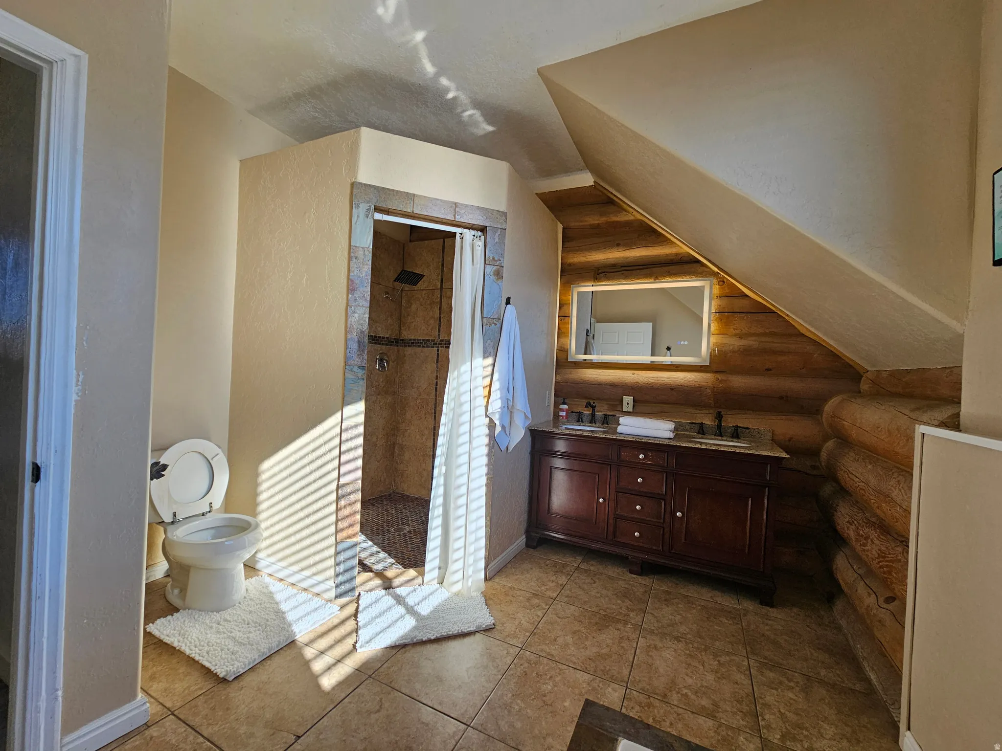 Bathroom with rustic walls, a stall shower, double vanity, and tile patterned floors