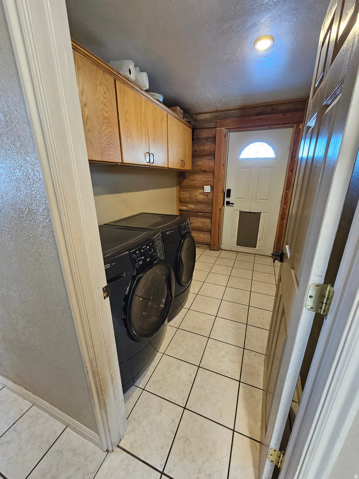 Laundry area with rustic walls, a textured ceiling, independent washer and dryer, cabinet space, and light tile patterned flooring