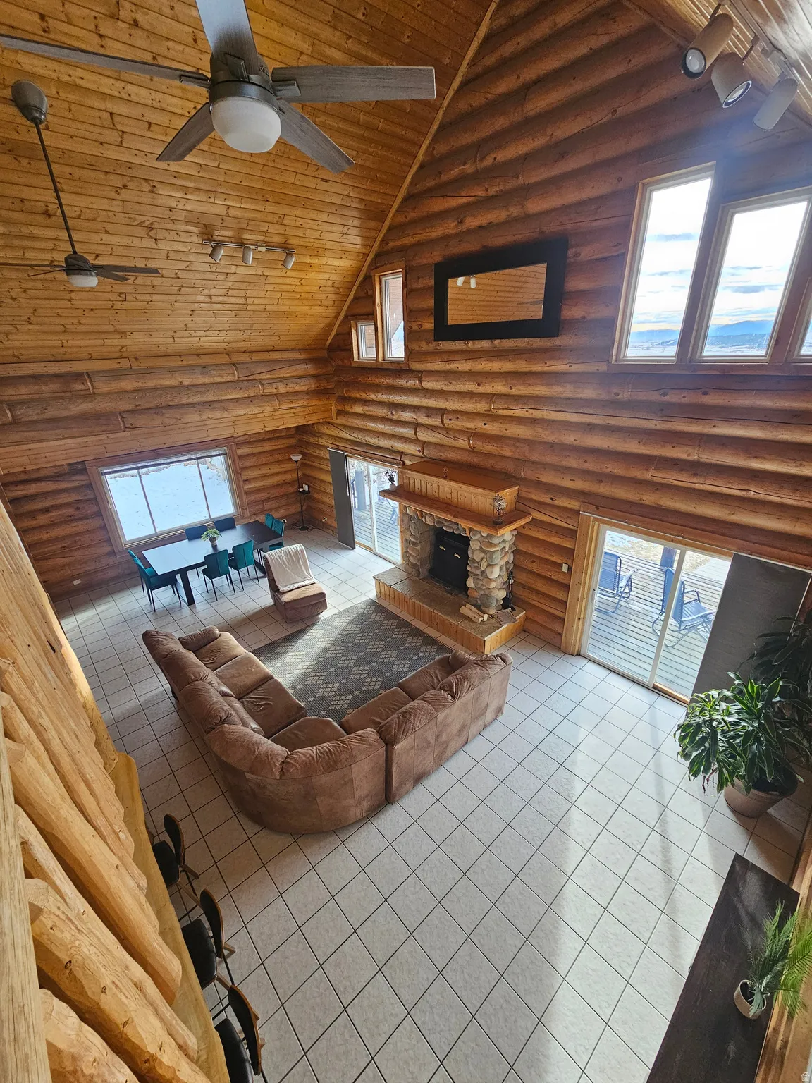 Tiled living room with a ceiling fan, rustic walls, and a vaulted wood ceiling