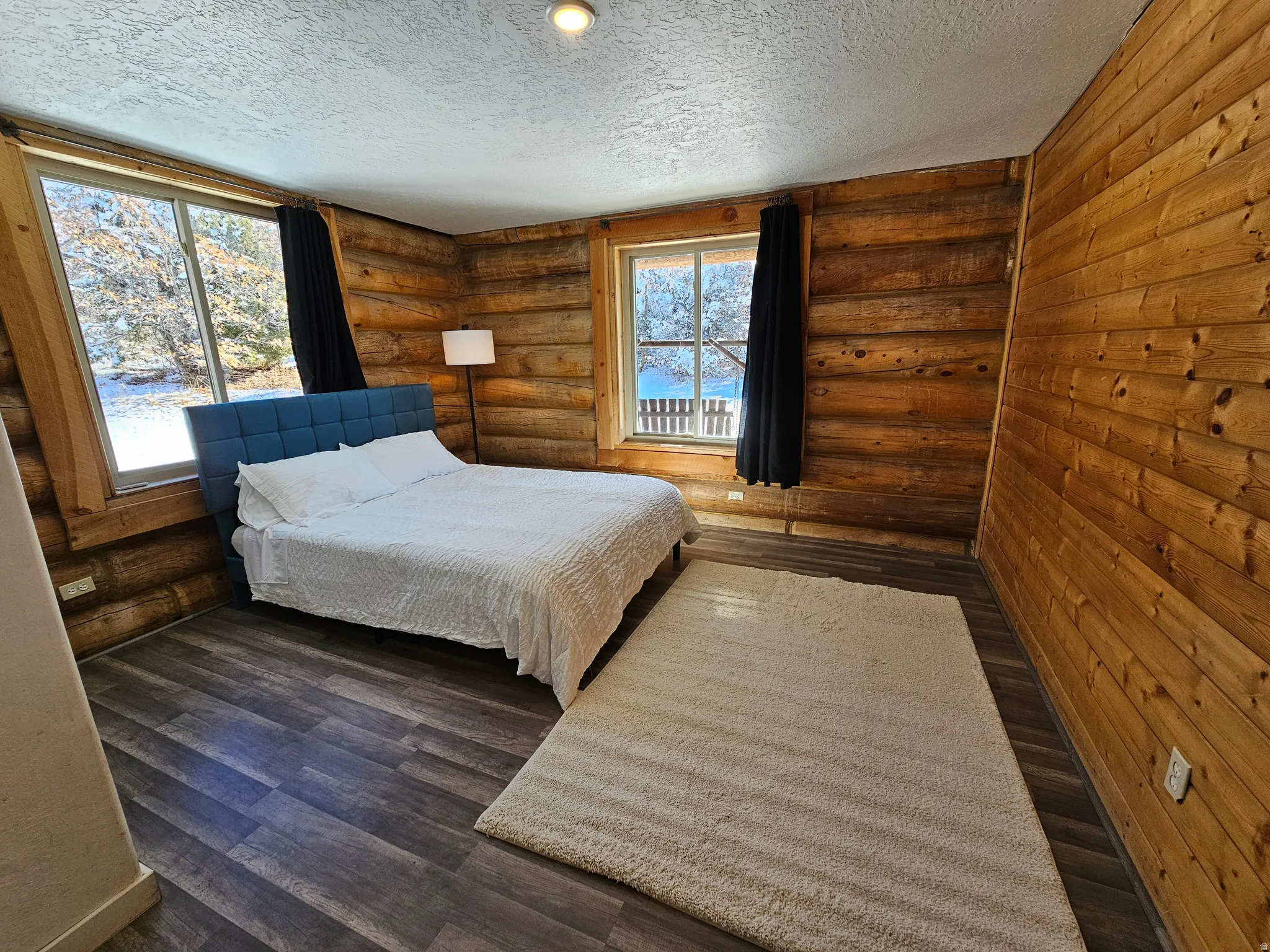 Bedroom featuring log walls, a textured ceiling, and wood finished floors
