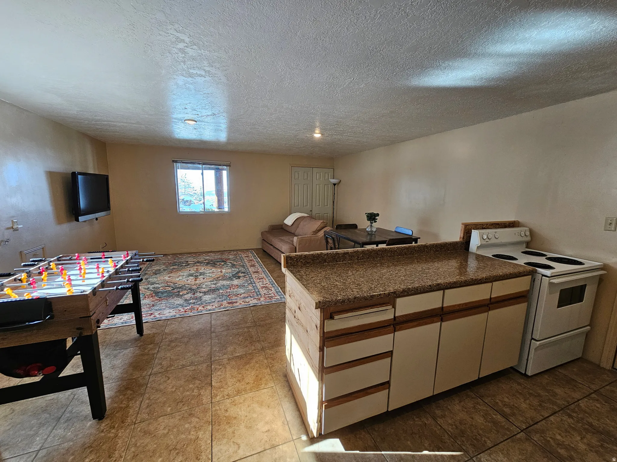 Kitchen featuring white electric range, a peninsula, dark countertops, a textured ceiling, and open floor plan
