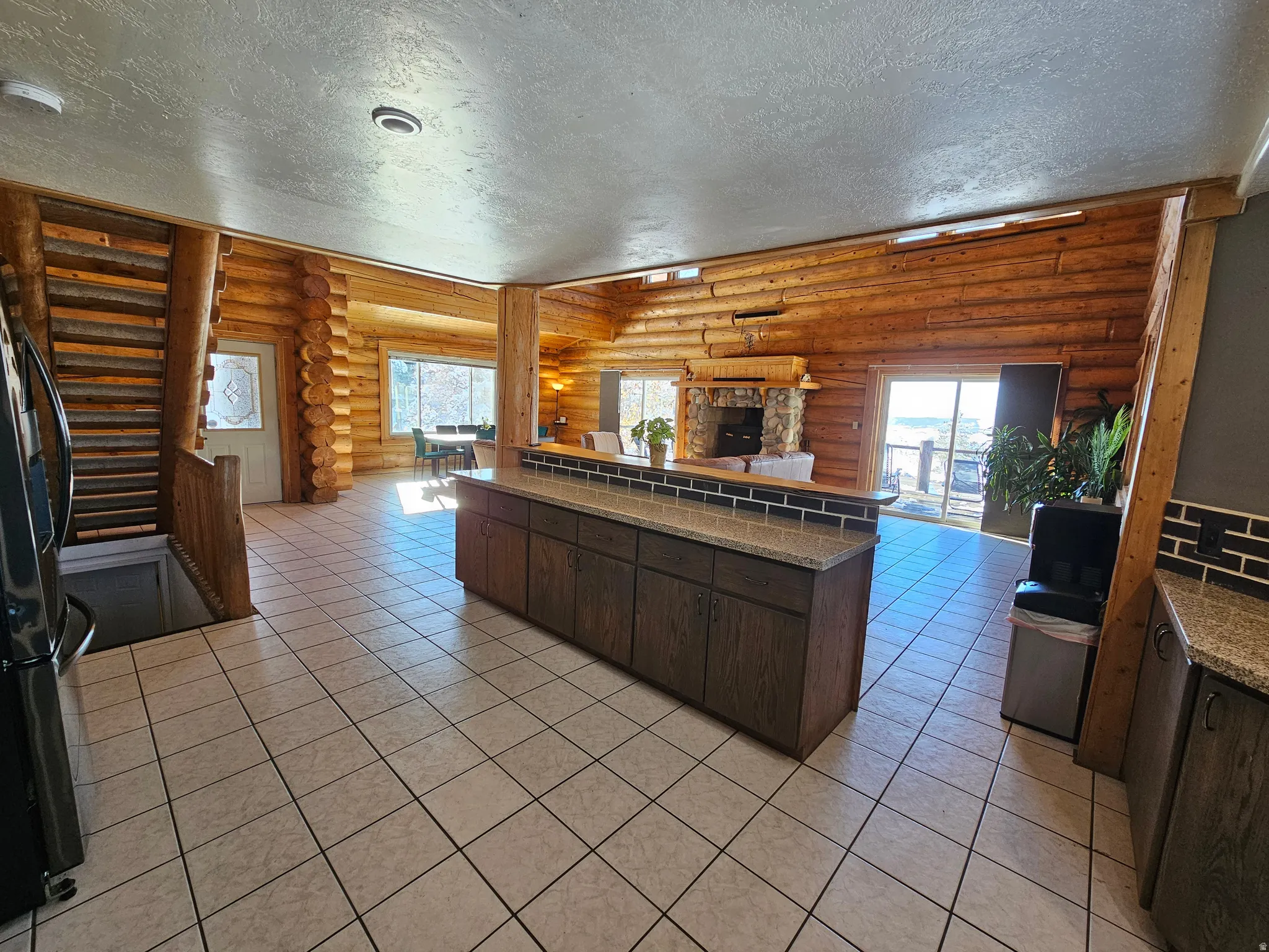 Kitchen with a textured ceiling, dark wood finish cabinets, open floor plan, rustic walls, and freestanding refrigerator