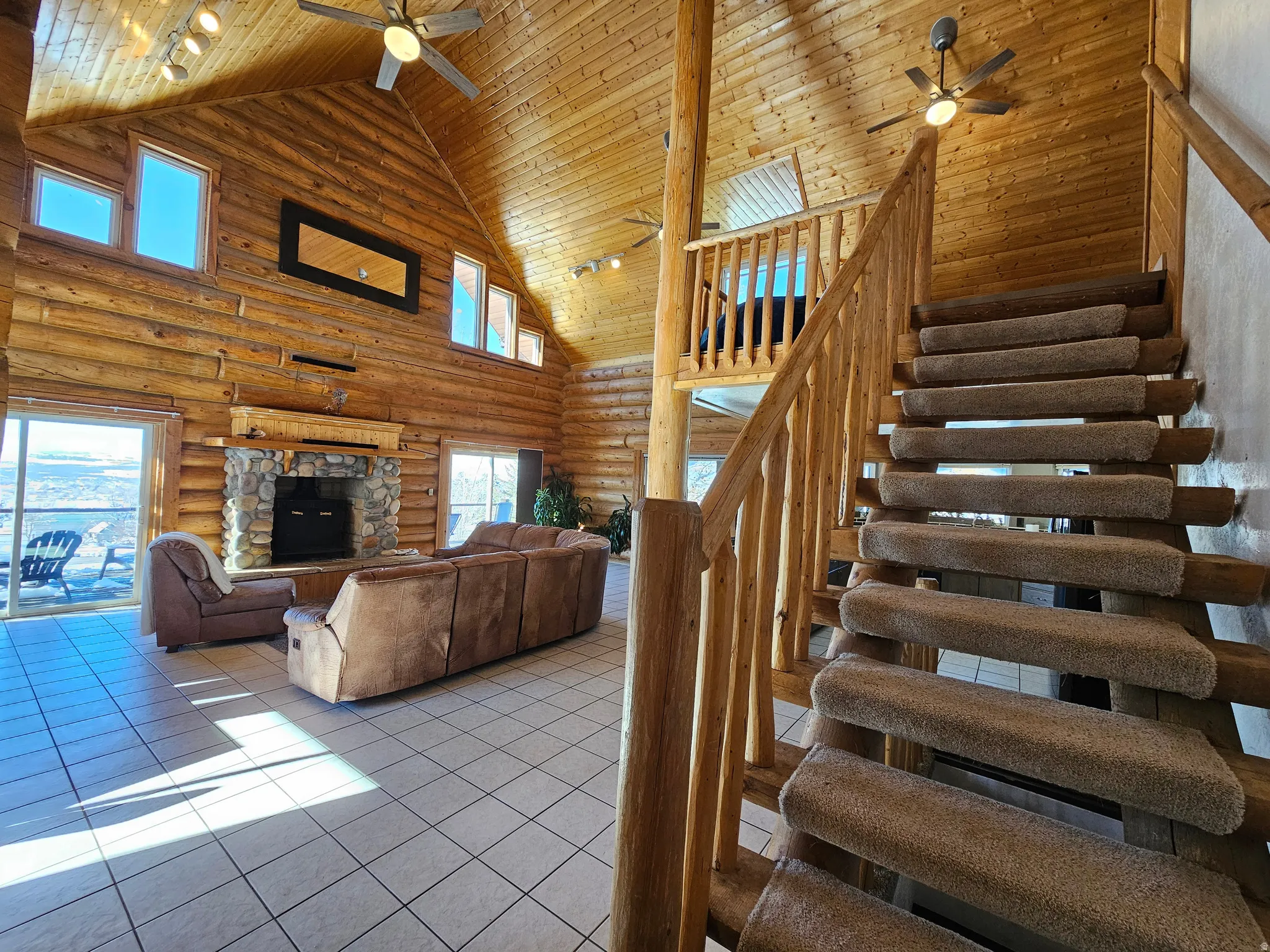 Stairs with ceiling fan, a high wooden ceiling, rail lighting, log walls, and tile patterned floors