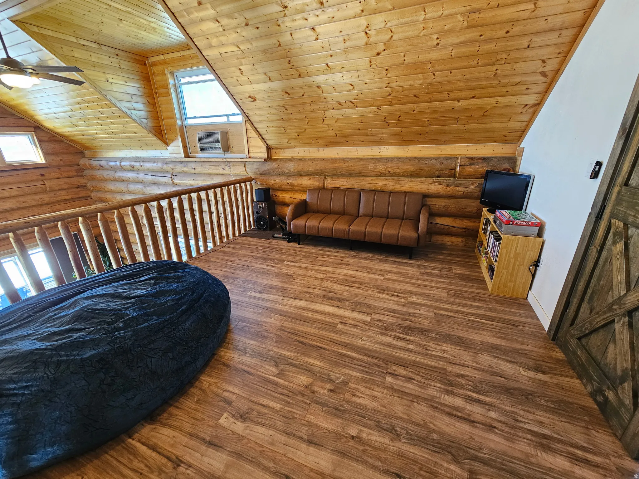 Additional living space featuring log walls, a ceiling fan, a vaulted wooden ceiling, and hardwood / wood-style flooring