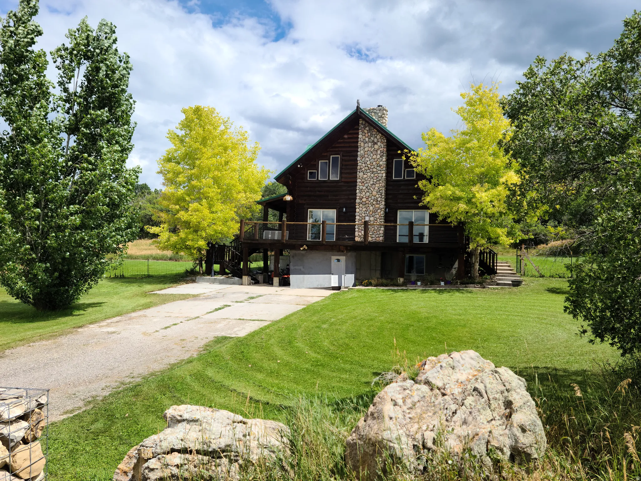 View of side of home featuring driveway, a deck, a chimney, and log siding