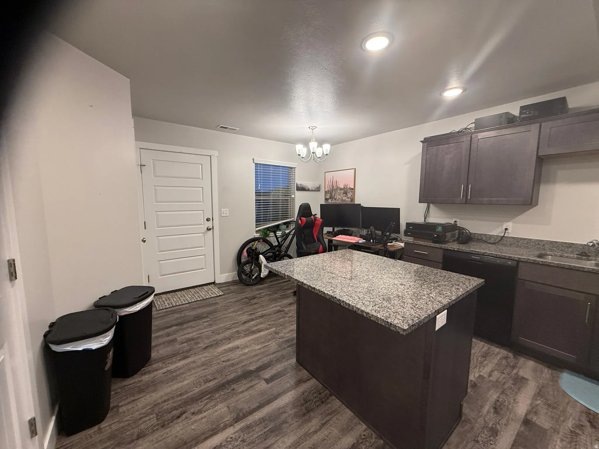 Kitchen featuring dark wood finish cabinets, a center island, hanging lights, dishwasher, and dark wood-type flooring