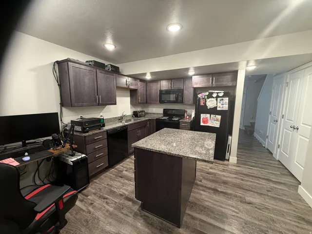 Kitchen with dark wood finish cabinetry, dark wood-style flooring, a kitchen island, and black appliances