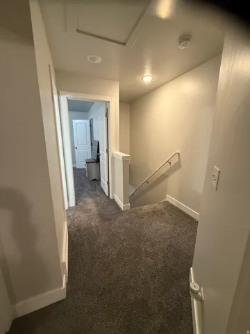 Corridor featuring an upstairs landing and dark carpet