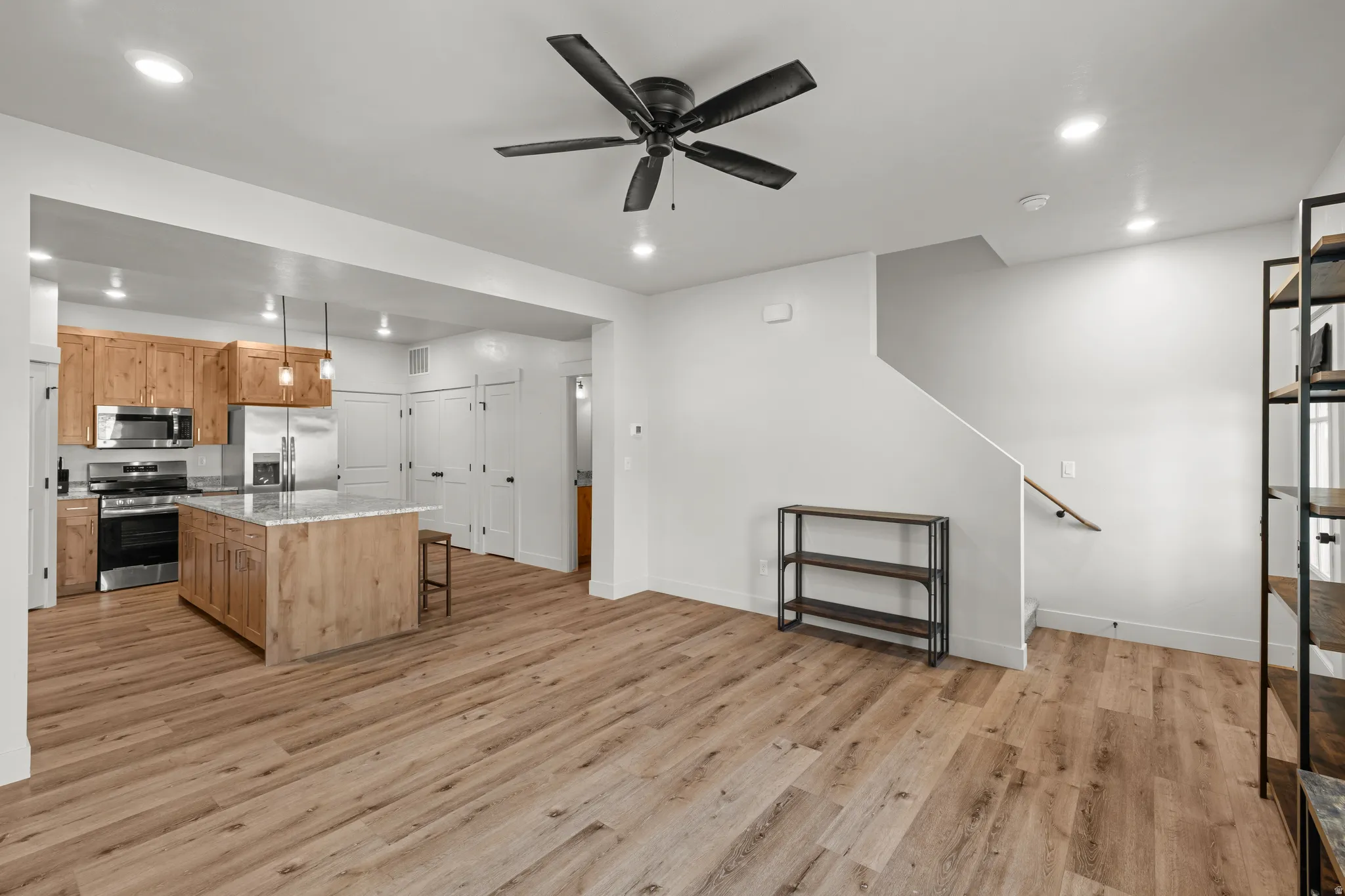 Kitchen with stainless steel appliances, a kitchen island, a ceiling fan, light wood-style flooring, and a kitchen breakfast bar