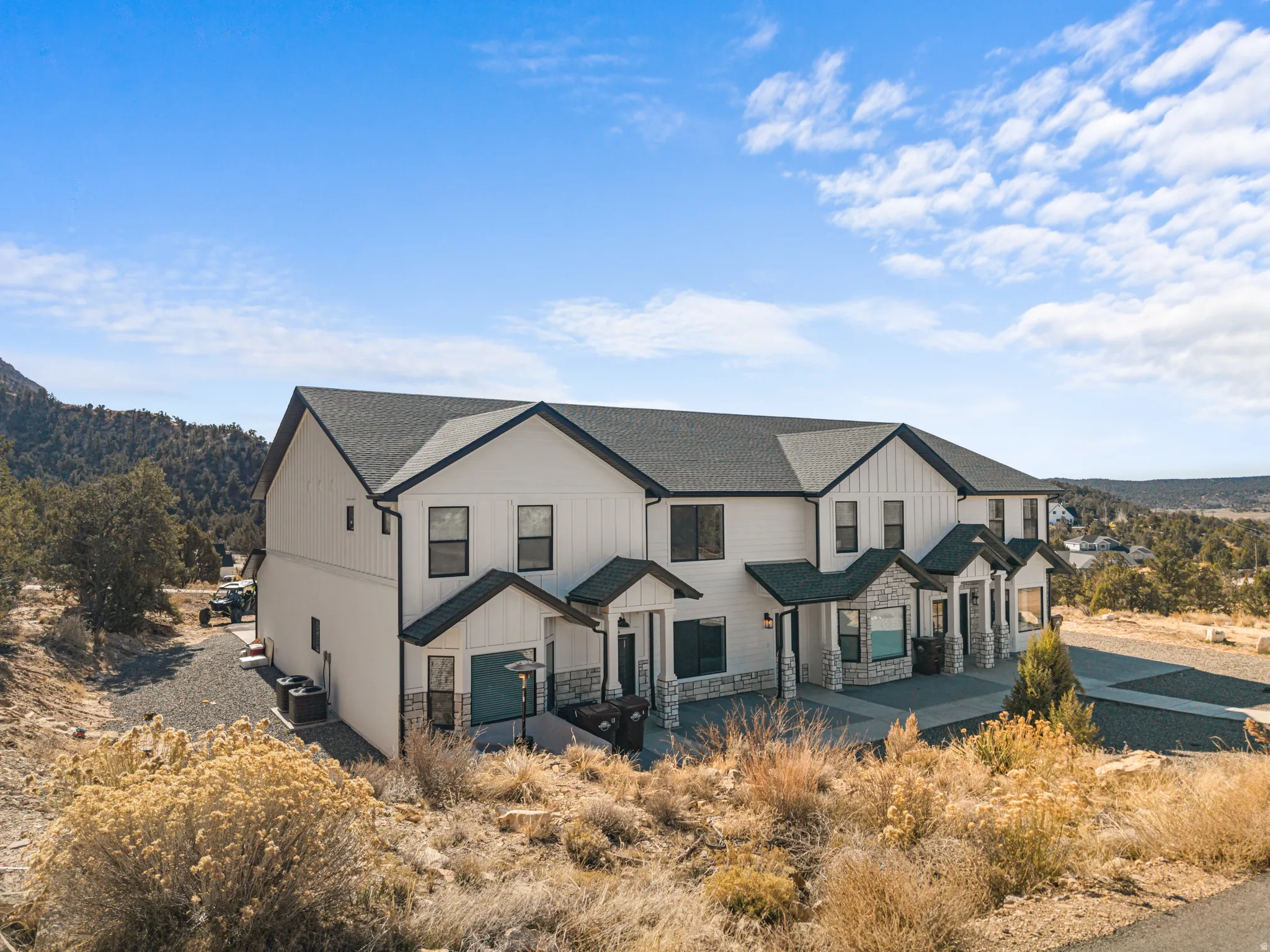 Modern farmhouse style condo building with stone siding, covered porch, and roof with shingles