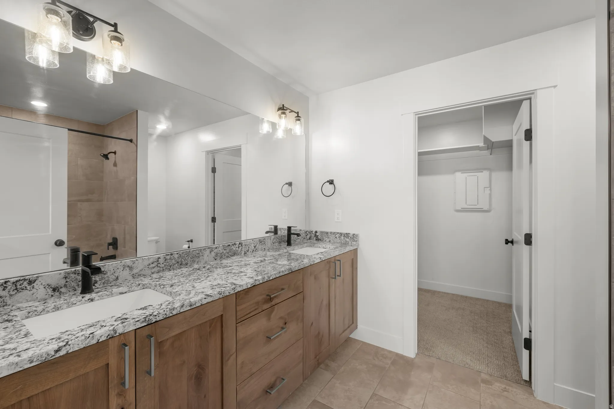 En suite bathroom featuring double vanity, a tile shower, light tile patterned floors, and a walk in closet