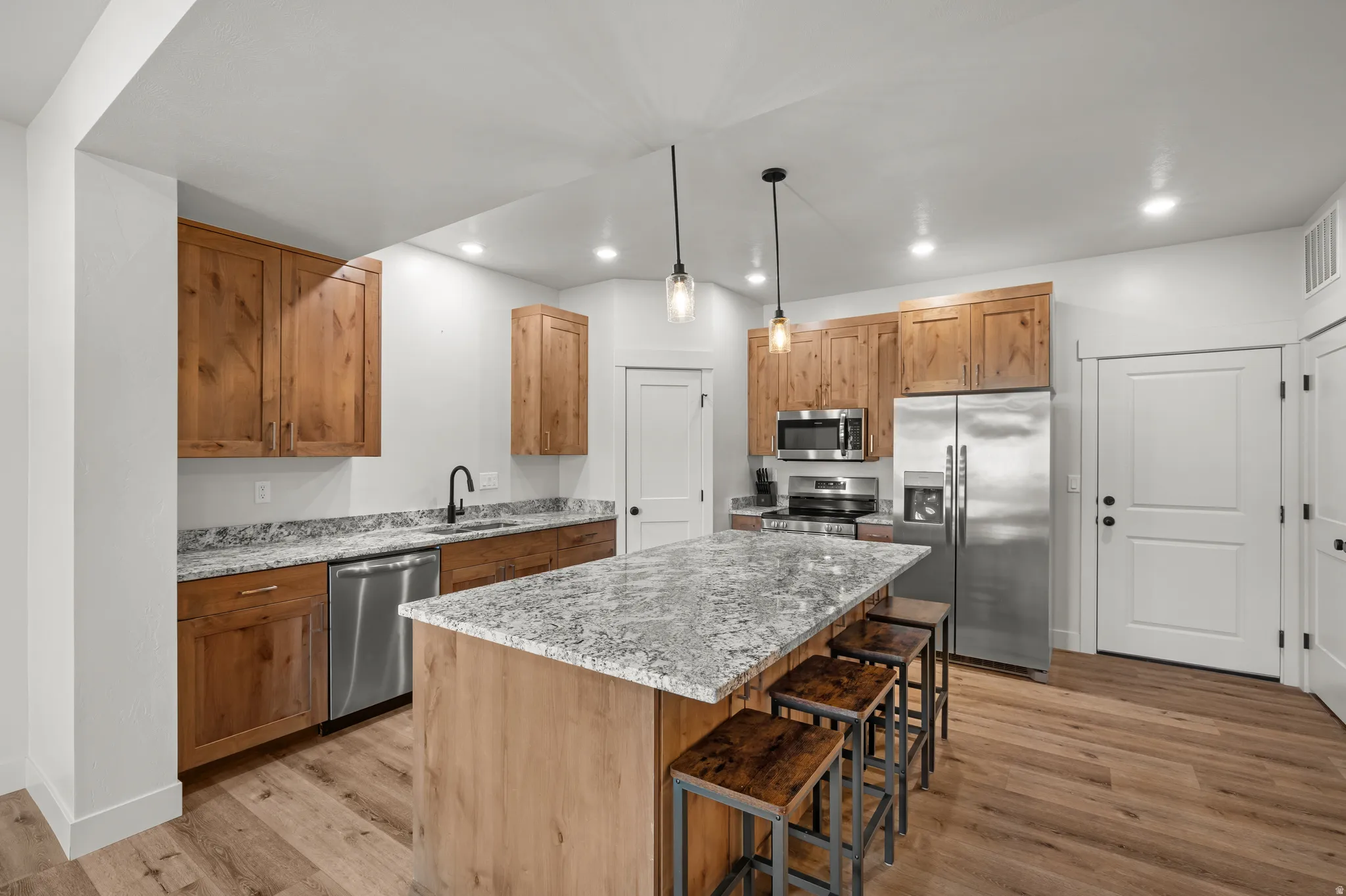Kitchen with light stone countertops, stainless steel appliances, pendant lighting, light wood-style flooring, and a kitchen bar