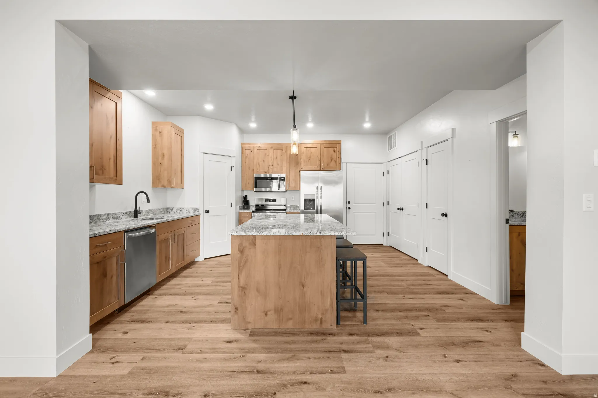 Kitchen featuring light stone countertops, a center island, hanging light fixtures, light wood finished floors, and stainless steel appliances