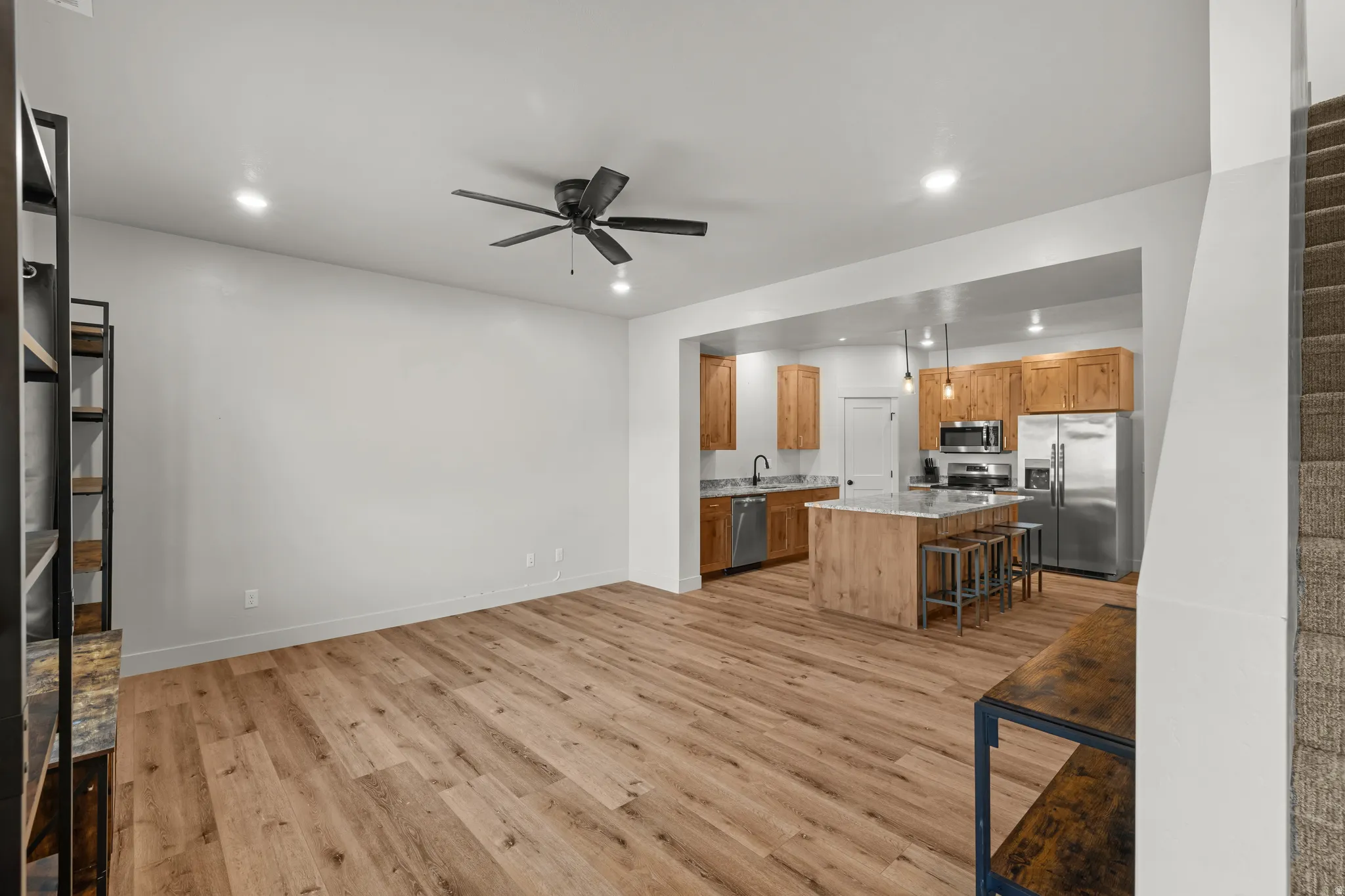 Kitchen with stainless steel appliances, a ceiling fan, light wood finished floors, a kitchen island, and a kitchen breakfast bar