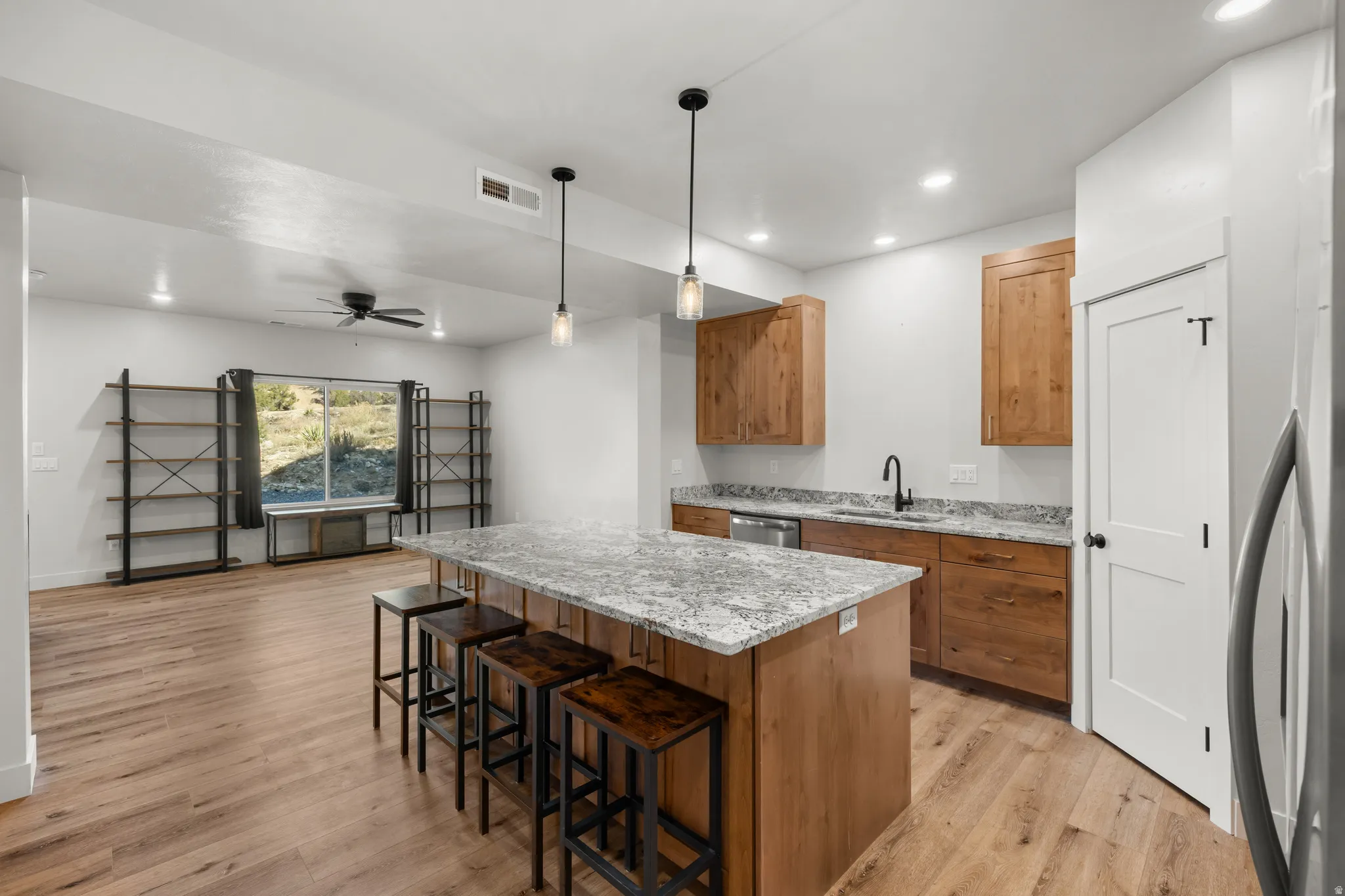 Kitchen with wood finish cabinets, hanging light fixtures, a center island, light stone countertops, and light wood-style floors