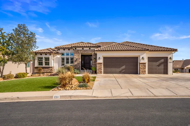 Mediterranean / spanish-style house with stone siding, an attached garage, driveway, stucco siding, and a front lawn