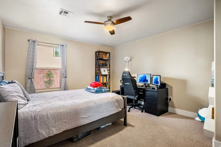 Carpeted bedroom featuring ceiling fan and an office area