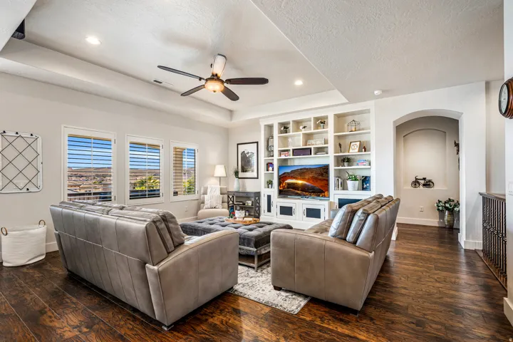 Living room featuring a ceiling fan, a tray ceiling, dark wood-style floors, built in shelves, and a textured ceiling