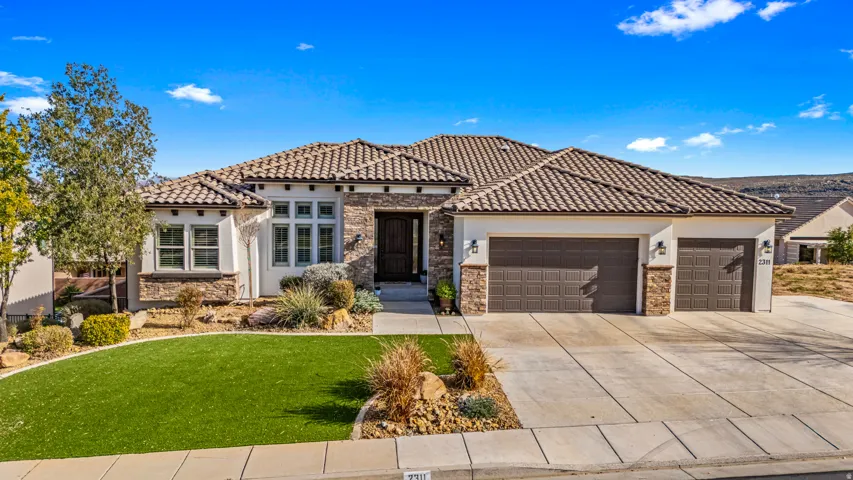 Mediterranean / spanish house with a front lawn, a garage, concrete driveway, and stone siding