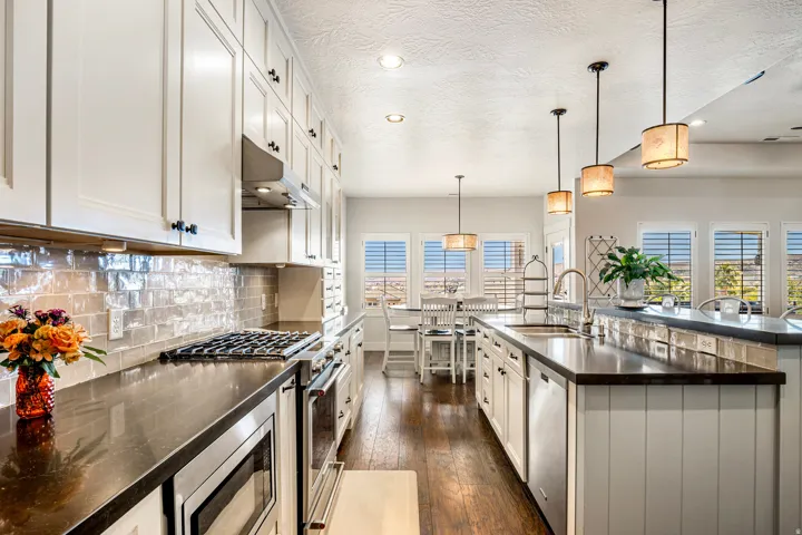 Kitchen with stainless steel appliances, dark wood-style flooring, pendant lighting, backsplash, and white cabinetry
