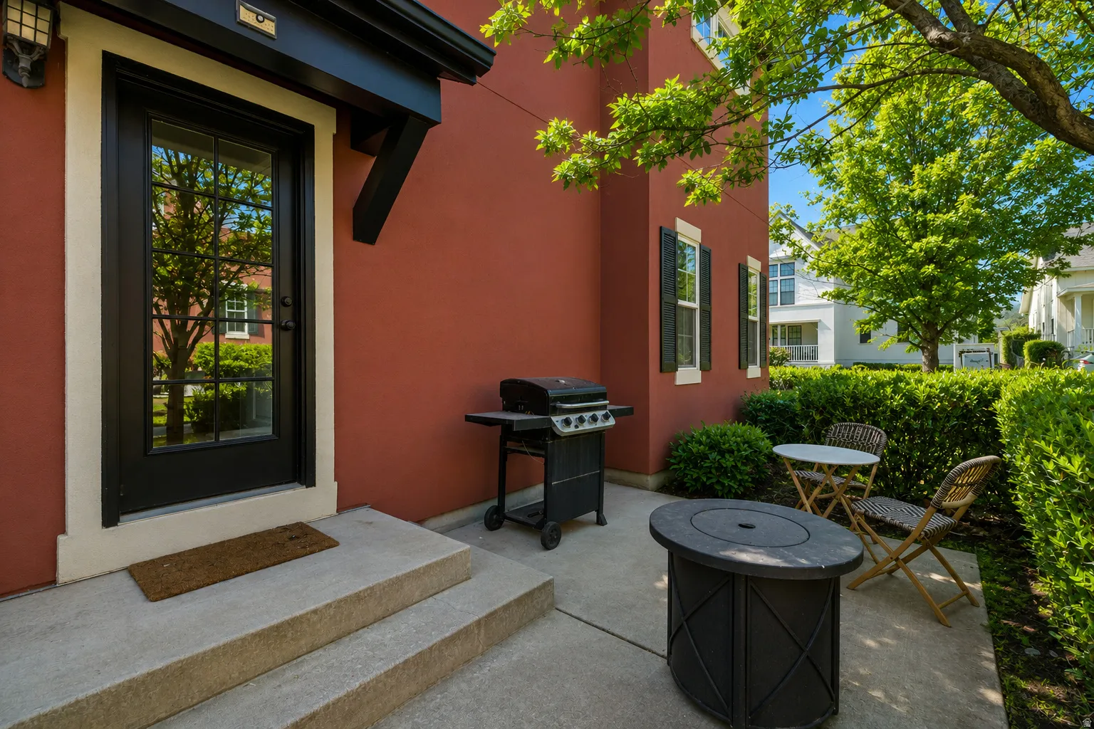 Red stucco exterior with a black grid-paneled entry door, framed by light trim and a dark awning