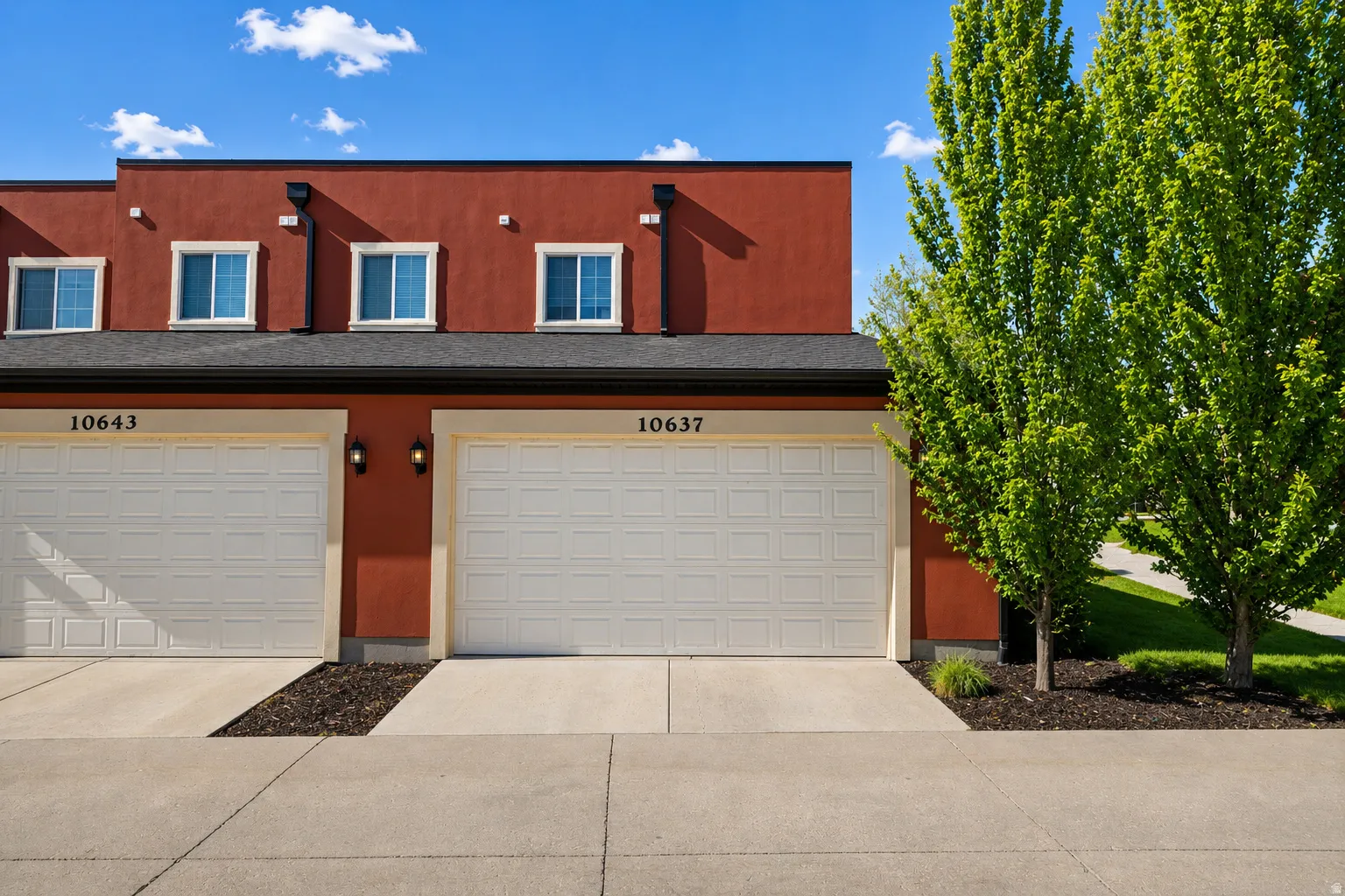 Red stucco exterior with white garage doors and white-framed windows
