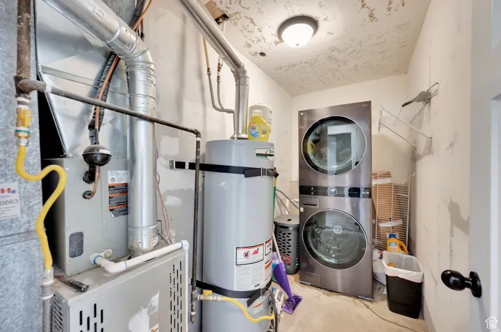 Laundry area with water heater, heating unit, stacked washer and dryer, and unfinished concrete flooring