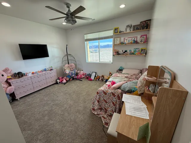 Carpeted interior room featuring a ceiling fan with integrated lighting, recessed ceiling lights, and a window with blinds