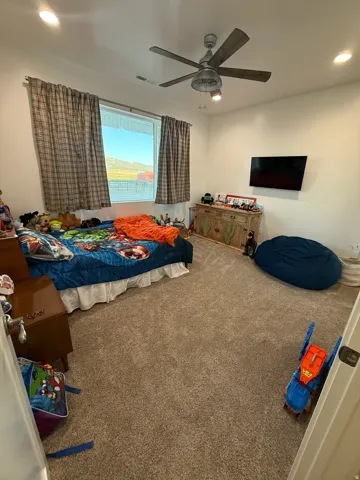 Spacious room featuring neutral carpeting, a large window, and a ceiling fan with integrated lighting