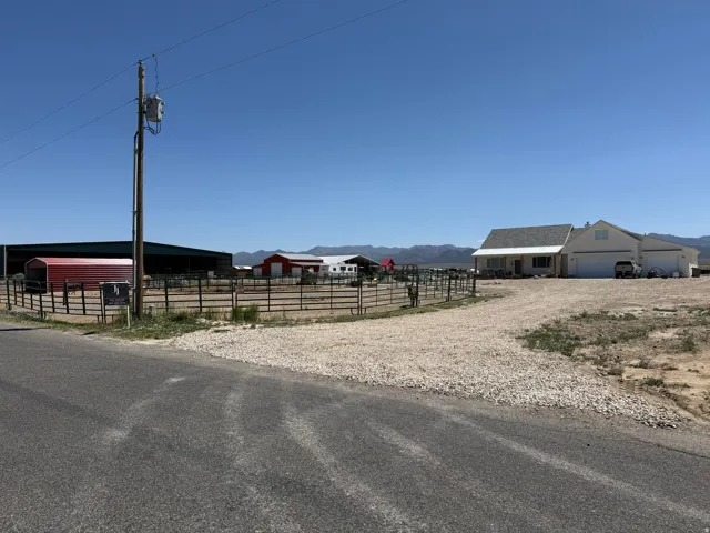 Expansive property featuring a modern ranch-style home with an attached garage, gravel driveway, and multiple outbuildings including a large barn and red-sided structures