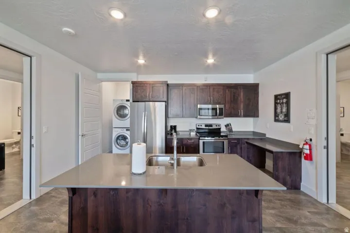 Kitchen with dark wood finish cabinetry, stainless steel appliances, stacked washer and dryer, an island with sink, and a breakfast bar area
