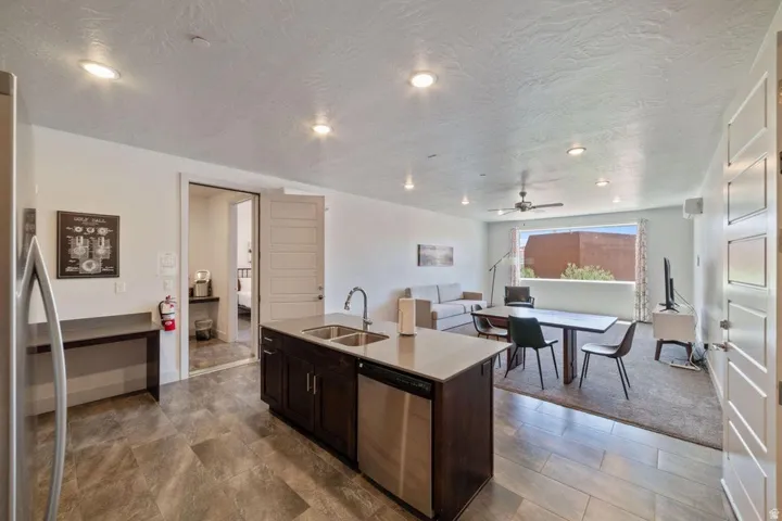 Kitchen featuring dark wood finish cabinets, stainless steel appliances, a center island with sink, open floor plan, and light stone countertops