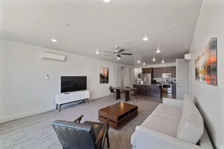 Living room featuring ceiling fan, light colored carpet, stacked washer and clothes dryer, a textured ceiling, and recessed lighting