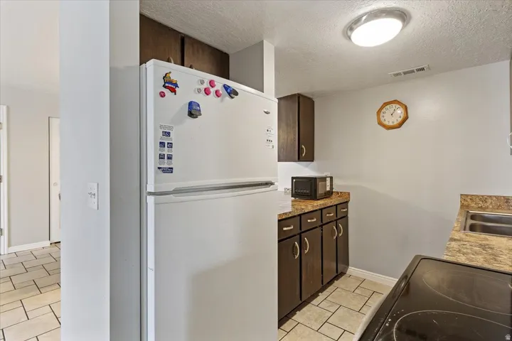 Kitchen featuring dark wood finish cabinets, black appliances, a textured ceiling, and light tile patterned floors