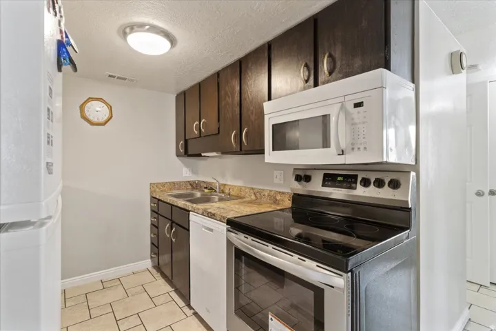 Kitchen with white appliances, dark wood finish cabinetry, a textured ceiling, light countertops, and light tile patterned floors