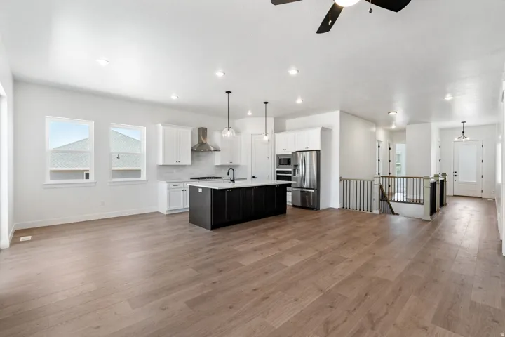 Kitchen with open floor plan, an island with sink, hanging light fixtures, stainless steel appliances, and two tone cabinetry