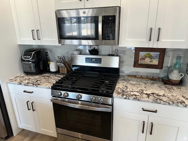 Kitchen featuring stainless steel appliances, white cabinets, light stone countertops, and backsplash