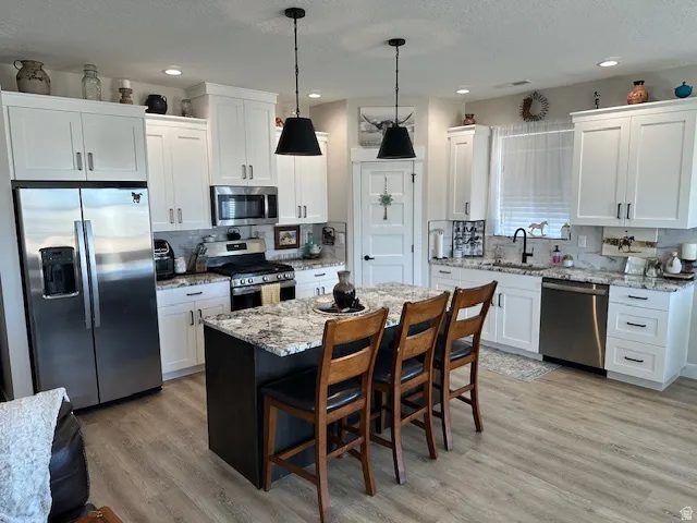 Two tone kitchen with stainless steel appliances, light stone countertops, a kitchen bar, a center island, and pendant lighting
