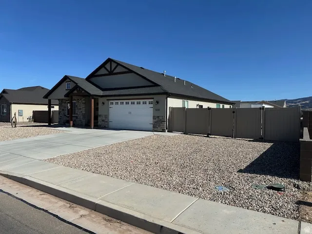 View of front of home with a gate, driveway, stone siding, an attached garage, and stucco siding