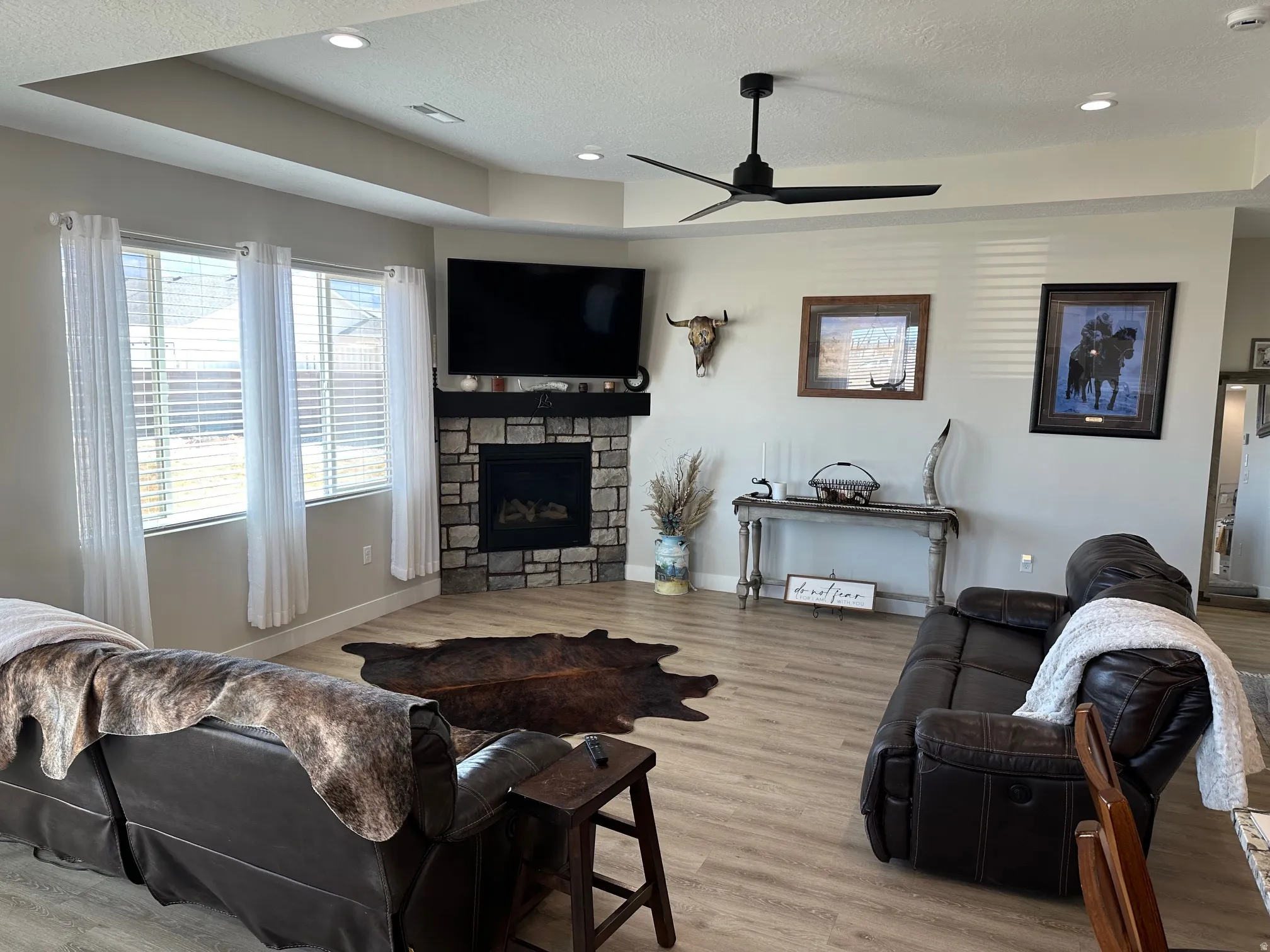 Living room featuring light wood-style flooring, a ceiling fan, a textured ceiling, a stone fireplace, and recessed lighting