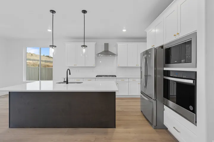 Kitchen featuring stainless steel appliances, a kitchen island with sink, hanging light fixtures, two tone cabinetry, and light wood-type flooring