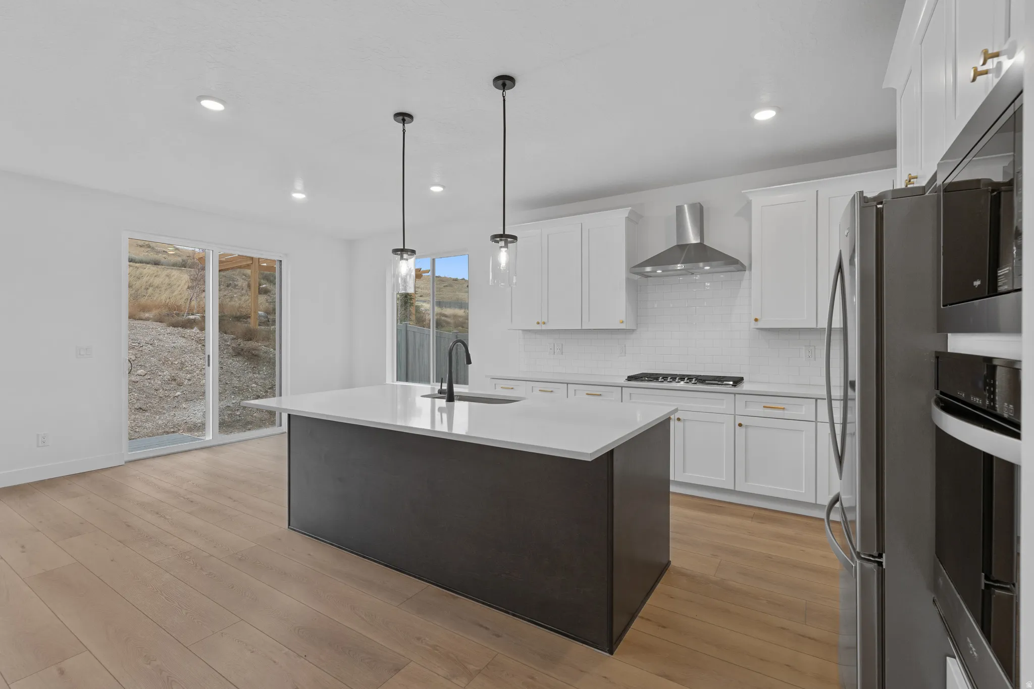 Kitchen featuring an island with sink, two tone cabinetry, stainless steel appliances, hanging light fixtures, and decorative backsplash