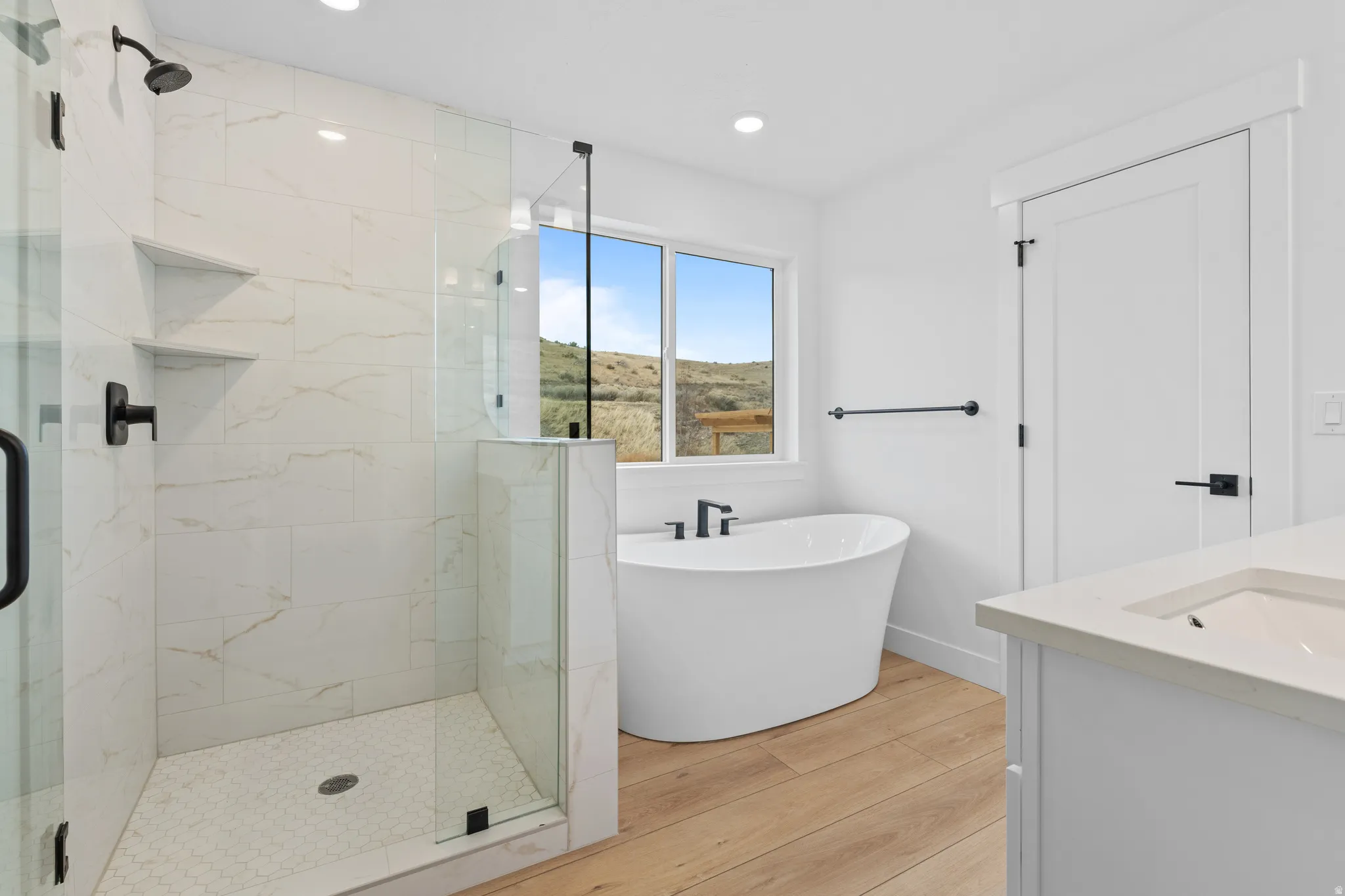 Full bath featuring a marble finish shower, a freestanding tub, light wood-style flooring, vanity, and recessed lighting